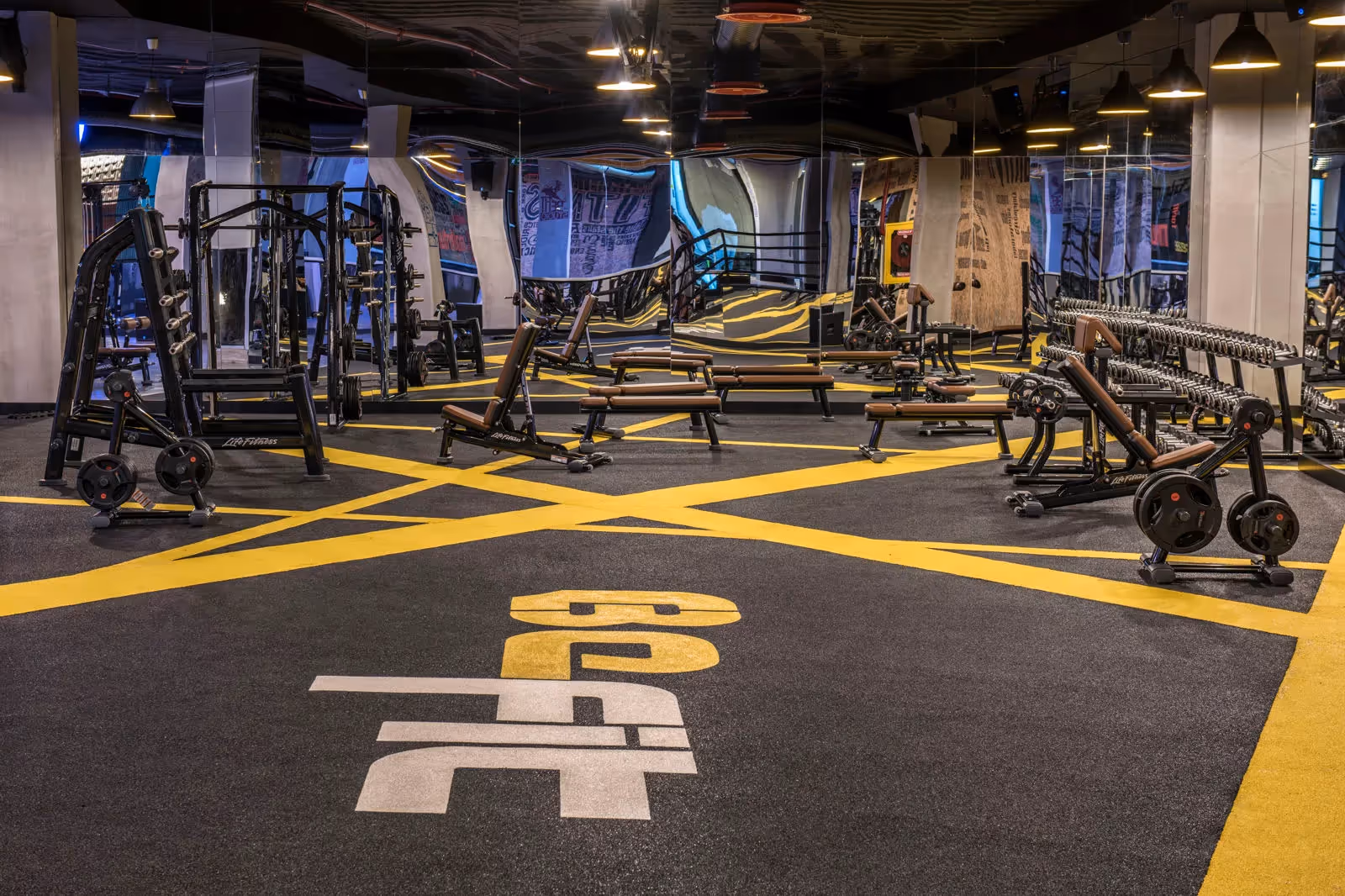 Krachtruimte met fitnessapparaten op een zwarte vloer met gele belijning in Delphin BE Grand Resort in Lara