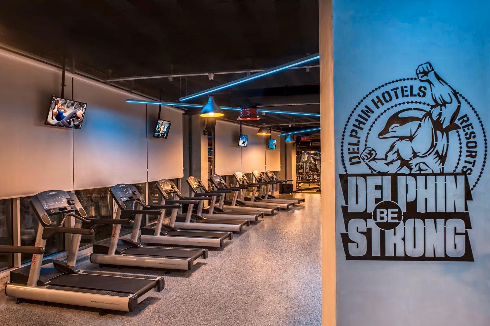 Fitnessruimte met een rij loopbanden en het logo Delphin Be Strong in Delphin BE Grand Resort in Lara