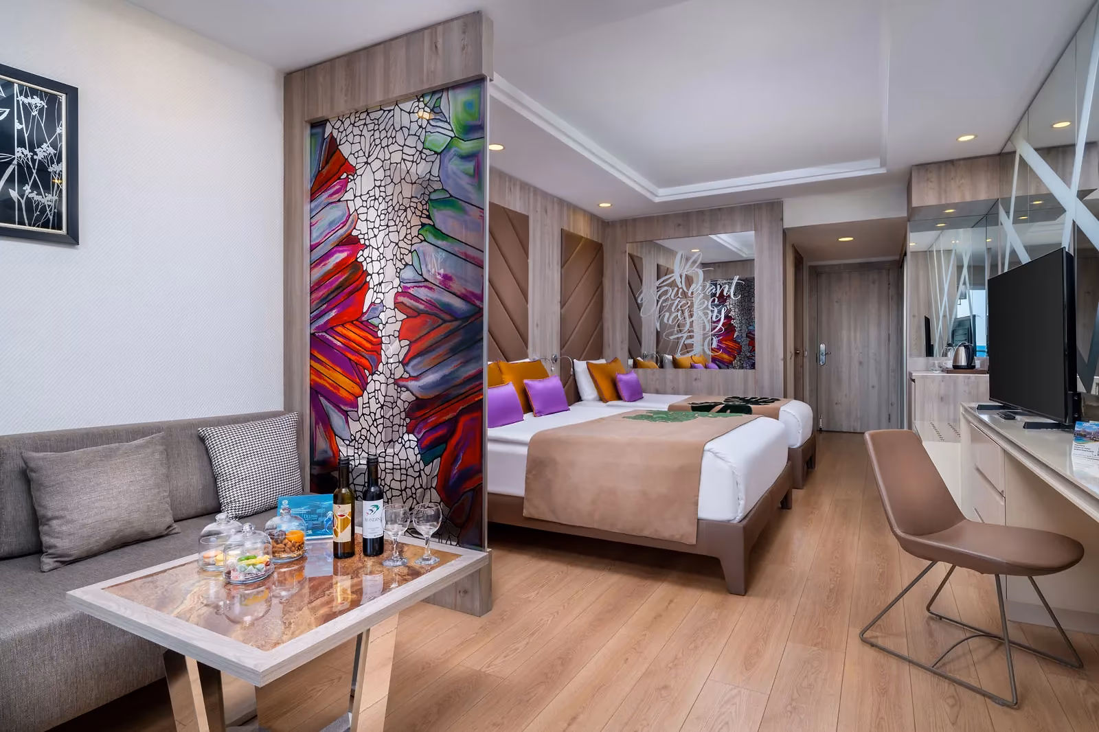 Standaardkamer van Delphin Be Grand met twee bedden, een bank, een salontafel en een kleurrijk kunstpaneel