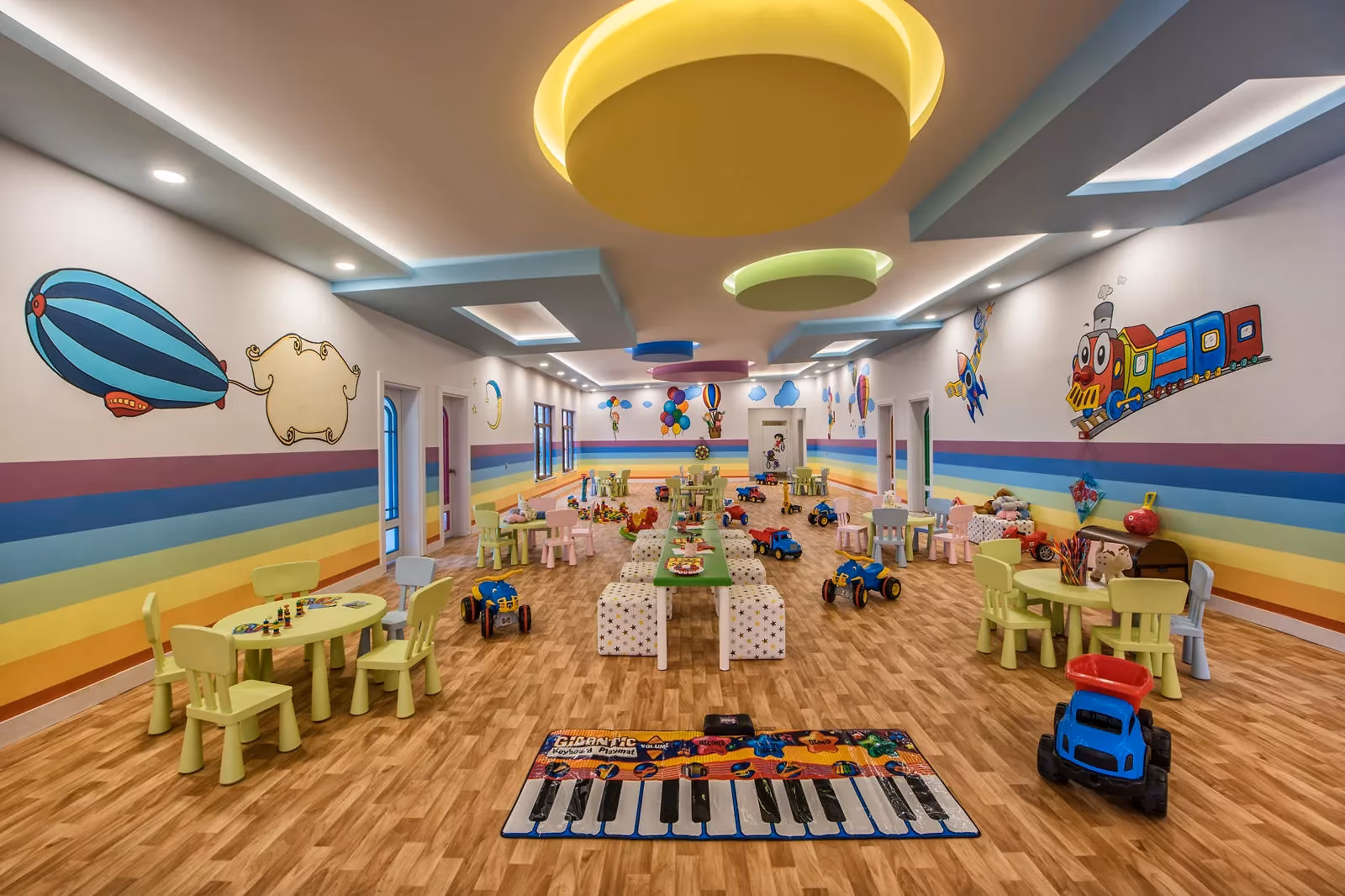 Binnenspeelzaal van de kinderclub van Delphin Be Grand met kindertafeltjes, speelgoedauto's en een vloerpiano