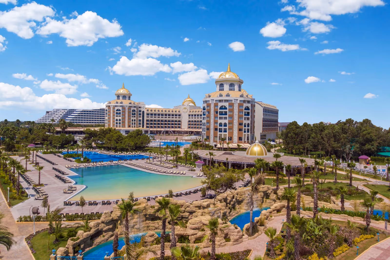 Lagunezwembad met zandstrandje, rotspartijen en palmen voor het hoofdgebouw van Delphin BE Grand Resort in Lara
