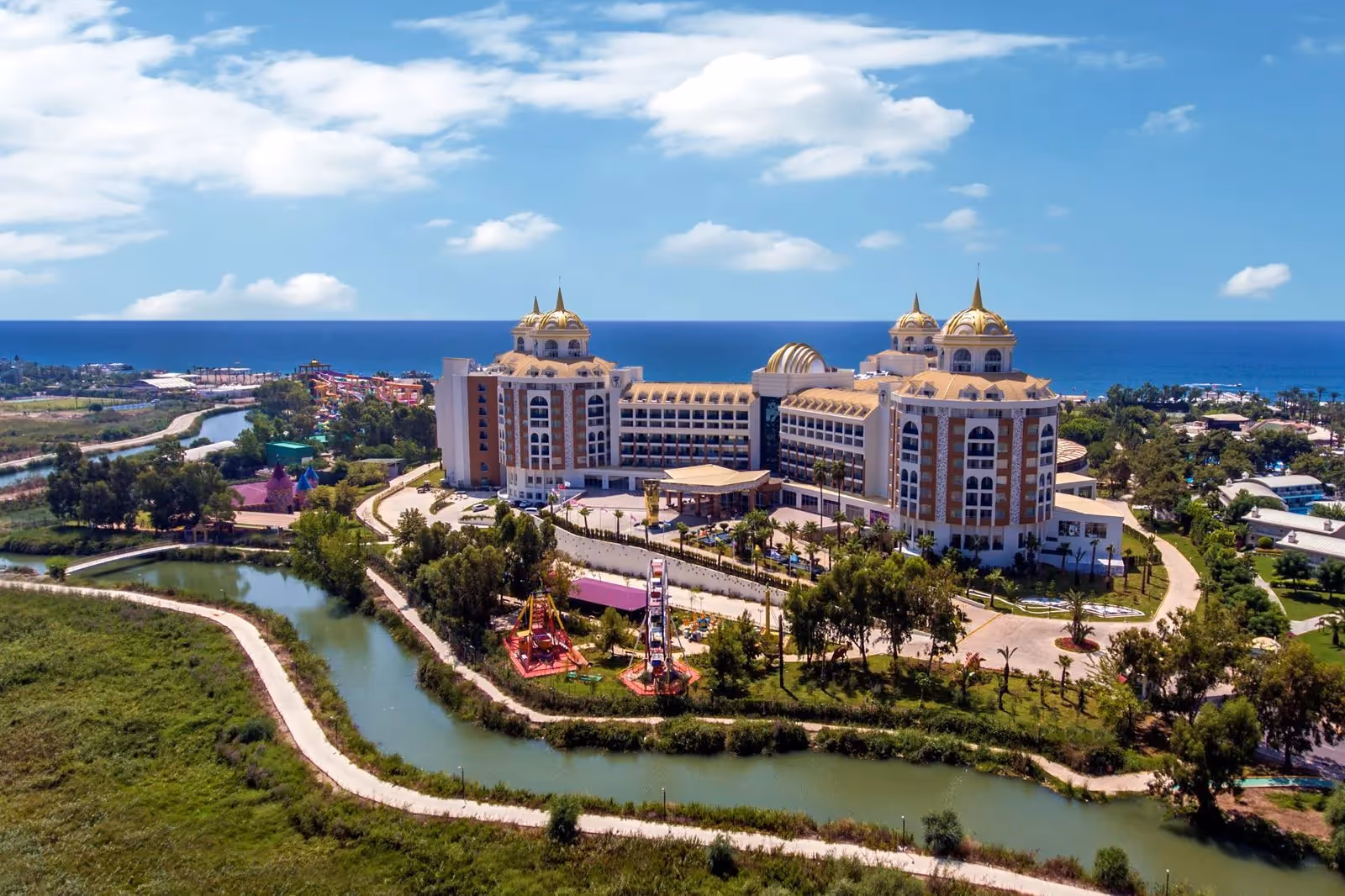 Luchtfoto van Delphin BE Grand Resort in Lara met de gebouwen met koepels, de groene tuinen en de rivier om het terrein, met de zee op de achtergrond