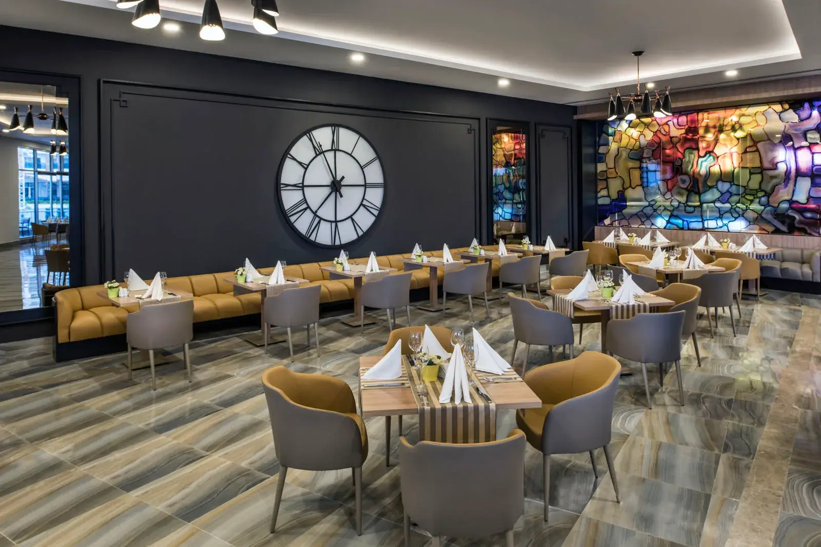 Restaurantzaal van Delphin Be Grand met gedekte tafels, een grote klok aan de wand en een glas-in-loodraam