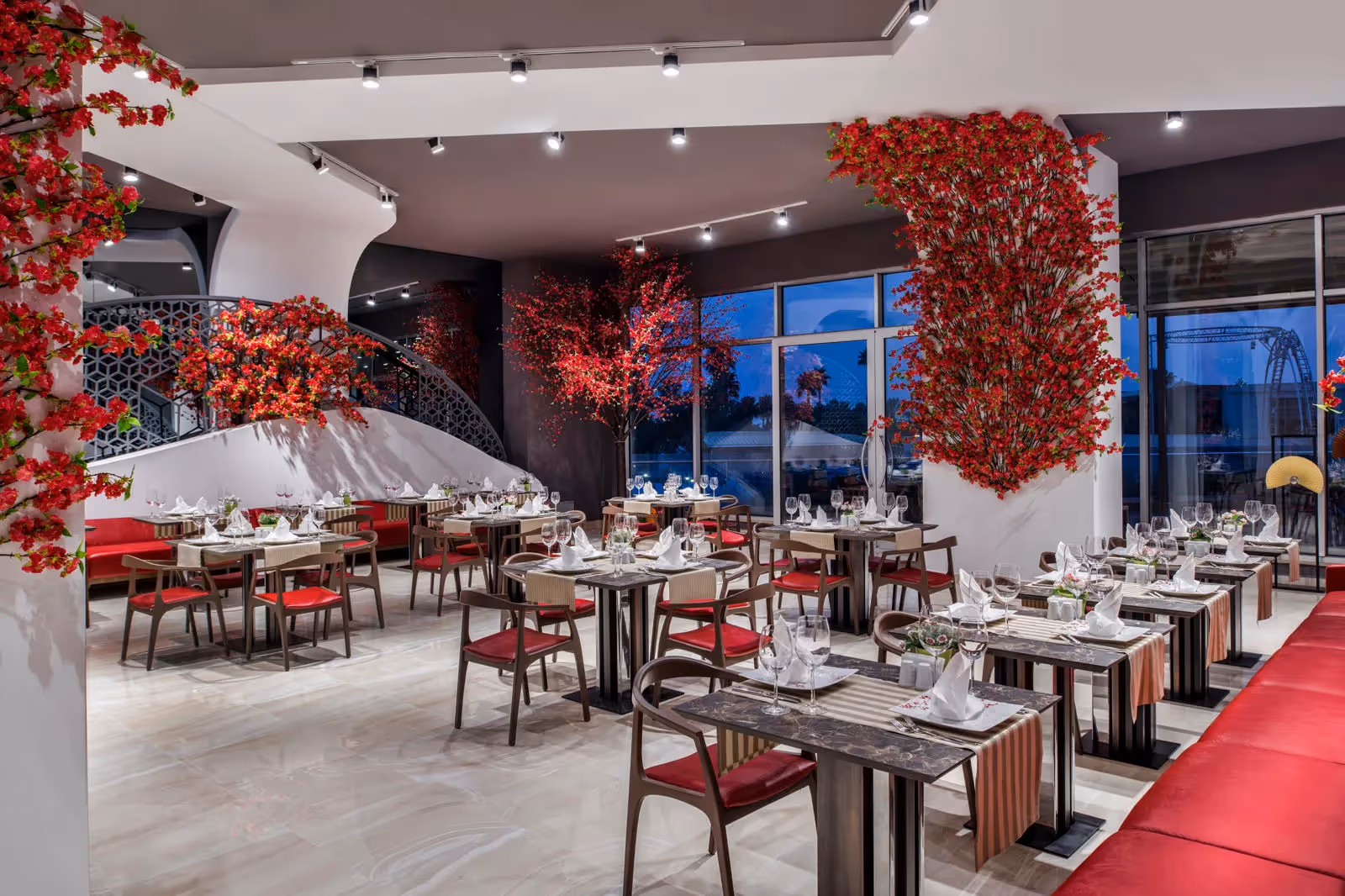 Restaurant met gedekte tafels, rode bloesemdecoratie en grote ramen in Delphin BE Grand Resort in Lara