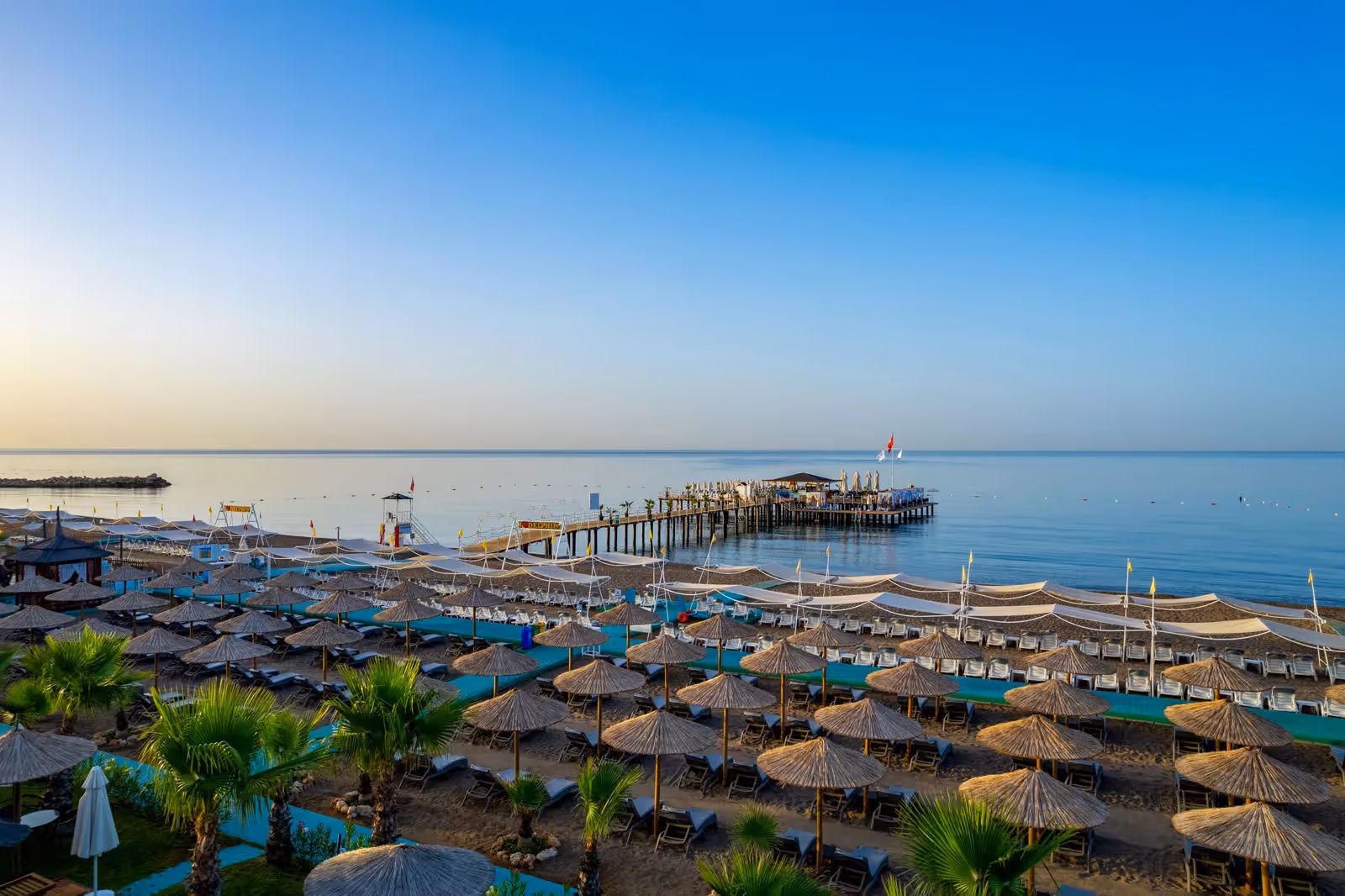 Zandstrand met rieten parasols en ligbedden en de pier in zee bij zonsondergang bij Delphin BE Grand Resort in Lara