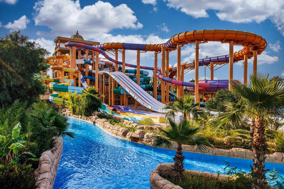 Hoge waterglijbanen van het aquapark boven de wildwaterbaan met palmen bij Delphin BE Grand Resort in Lara