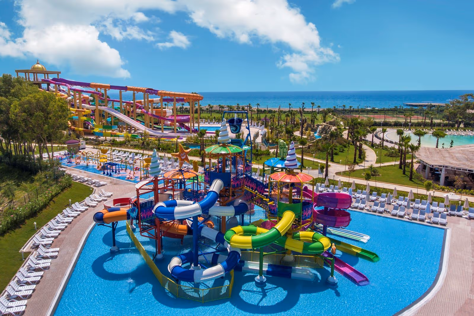 Waterspeeltoestel met glijbanen in een groot zwembad, met de zee op de achtergrond, bij Delphin BE Grand Resort in Lara