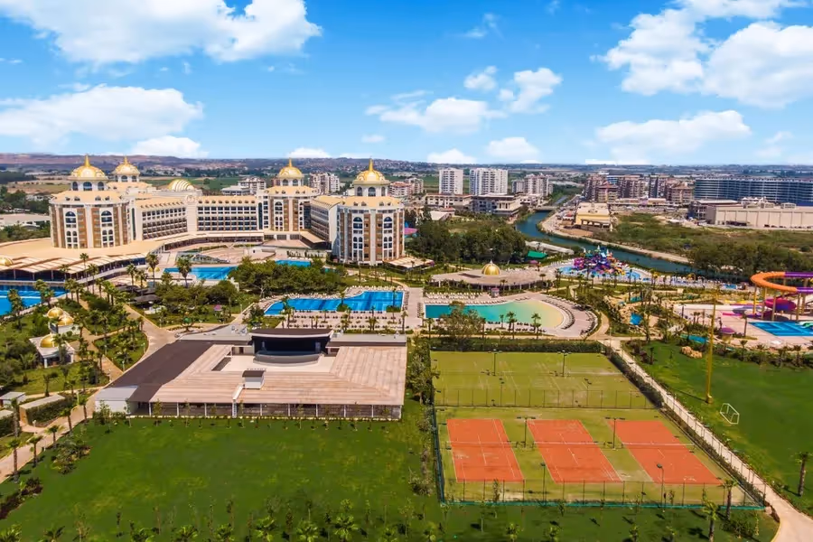 Luchtfoto van Delphin Be Grand Resort met de gebouwen met gouden koepels, de zwembaden, de tennisbanen en de rivier