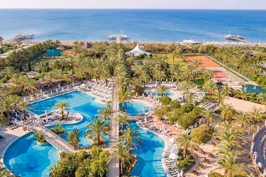 Zwembaden tussen palmbomen bij Hotel Royal Wings in Lara, met de zee erachter, van boven gezien